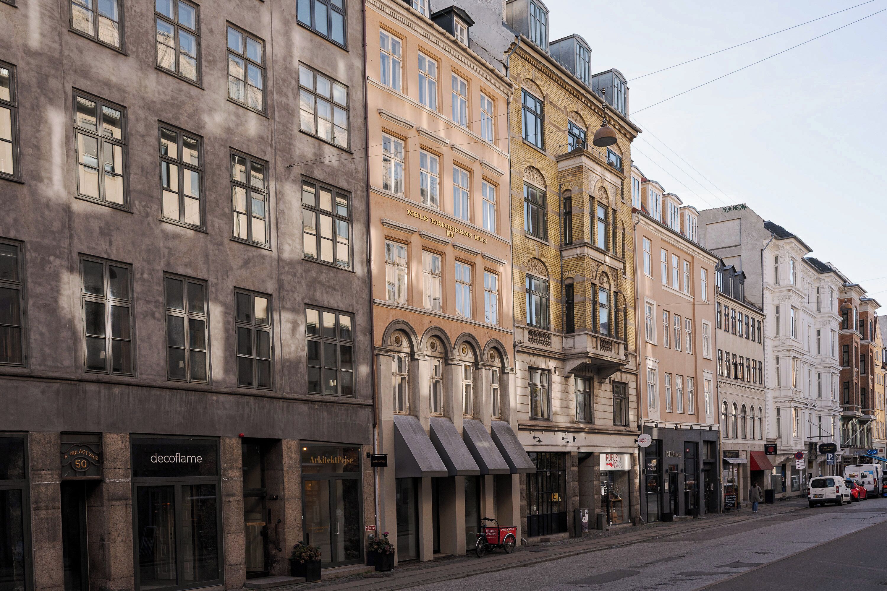 A row of historic buildings with storefronts, including a visible sign for 'Arkitekten Pejse'.