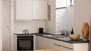 A modern kitchen with white cabinets, a black countertop, and a wooden bowl on the sink. - Kings48 by Daniel&Jacob's (Copenhagen)