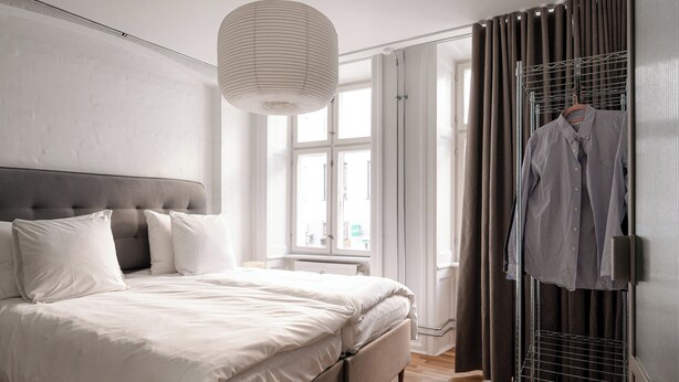 A modern bedroom with a large bed, a hanging light fixture, a wardrobe, and a window with curtains. - Kings48 by Daniel&Jacob's (Copenhagen)