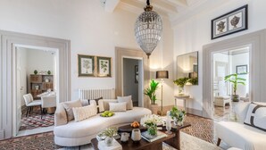 A spacious living room with a large sofa, a coffee table, and a chandelier. There are framed pictures on the walls and a dining area in the background. - The Fresco Tale a Charming 3 Bedrooms Apartment (Lucca)