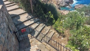 Un escalier en pierre, agrémenté d’une rampe métallique, mène à une falaise rocheuse qui surplombe la mer.