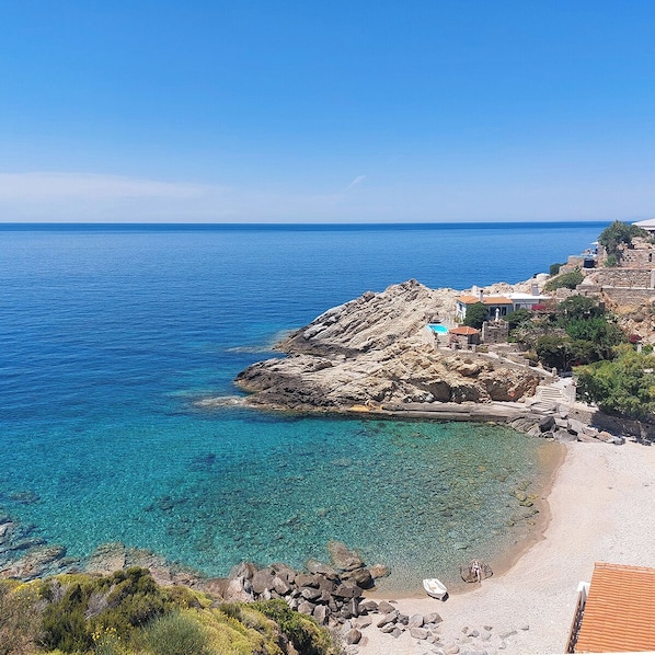 A coastal view with clear blue waters, rocky terrain, and a building with a blue roof.