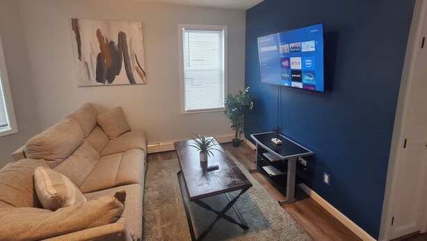 A living room with a beige sofa, a coffee table, a TV mounted on a blue wall, and a painting on the wall.