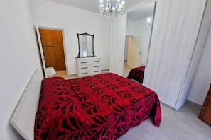 A bedroom with a bed, a dresser, a mirror, and a chandelier. - GuestHost - Comfortable Apartment Vallette Turin (Turin)