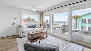 A spacious living room with a white sofa, a wooden coffee table, and a view of the balcony and outside. - Ocean View Escape in this 2 bedroom 2 bathroom Condo unit 5 (New Smyrna Beach)