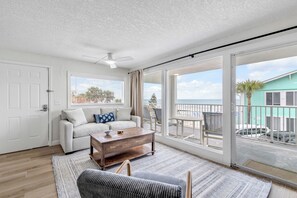 Amplia sala de estar con un sofá blanco, una mesa de centro de madera y vistas al balcón y al exterior.