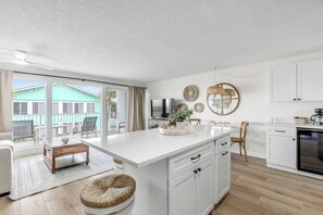 Une cuisine moderne dotée d’un grand îlot central, de meubles blancs et offrant une vue sur un bâtiment verdoyant à l’extérieur.
