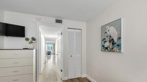 A room with a bed, a TV, a white dresser, a closet, and a painting on the wall. - Ocean View Escape in this 2 bedroom 2 bathroom Condo unit 5 (New Smyrna Beach)