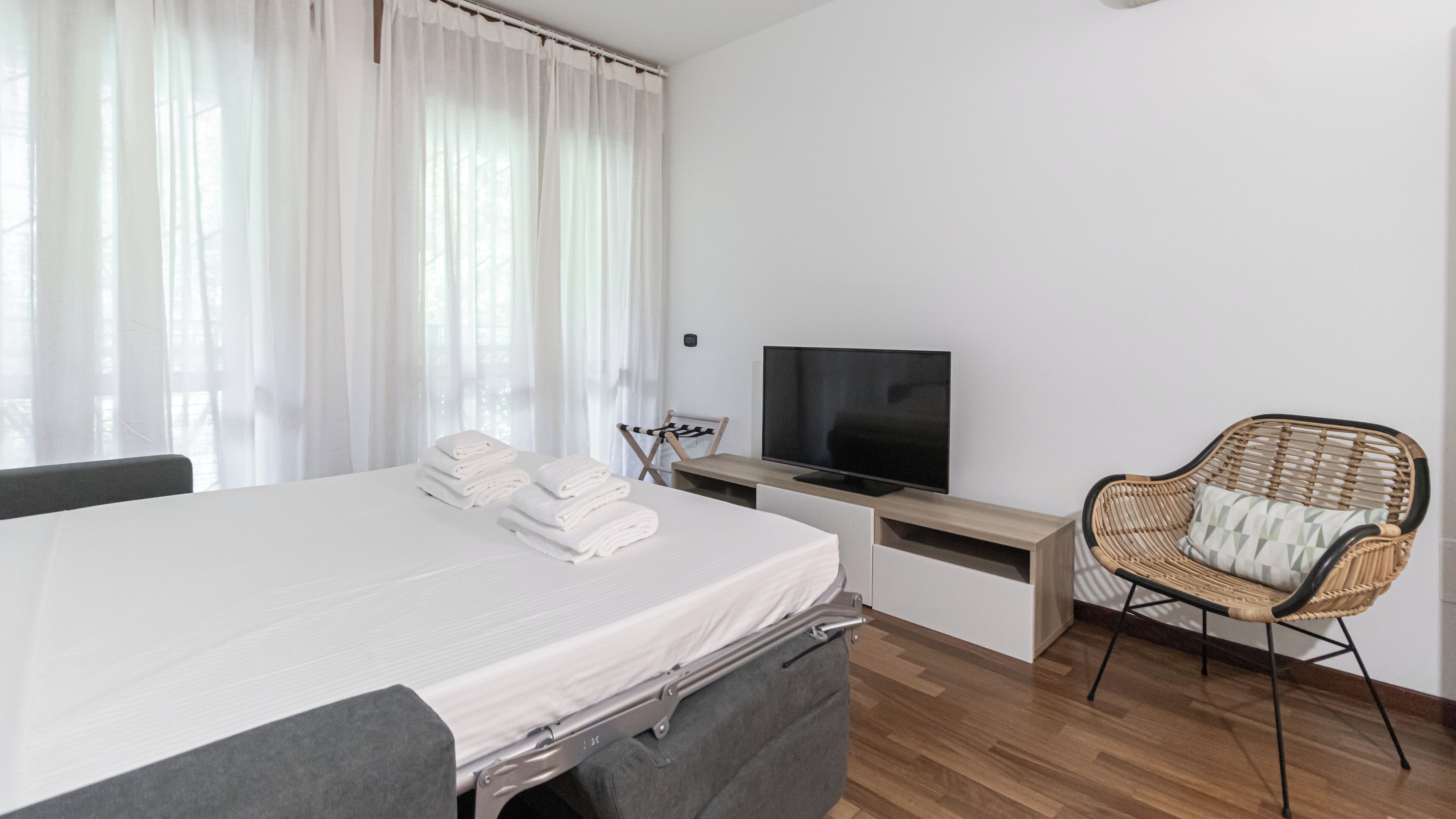 Une chambre d’hôtel avec un lit, une télévision, une chaise et une fenêtre avec des rideaux.