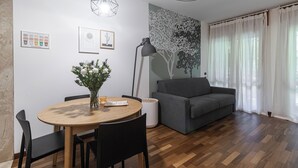 A modern living room with a round wooden dining table, black chairs, a grey sofa, and a wall-mounted lamp. - Italianway Comfort - Londonio 23 (Milano)