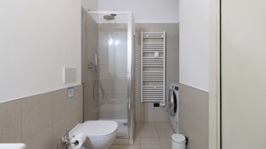 Casa de banho com chuveiro, sanita e um porta-toalhas.