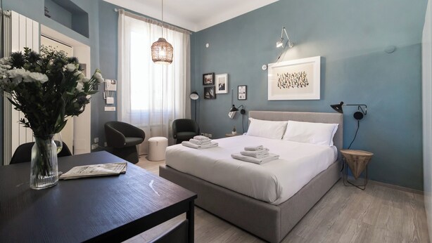 Ein modernes Schlafzimmer mit einem Bett, Nachttischen, einem Schreibtisch, Stühlen und einem Blumenstrauß.