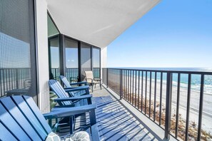 Un balcón con sillas Adirondack azules, una mesita y vista al mar.
