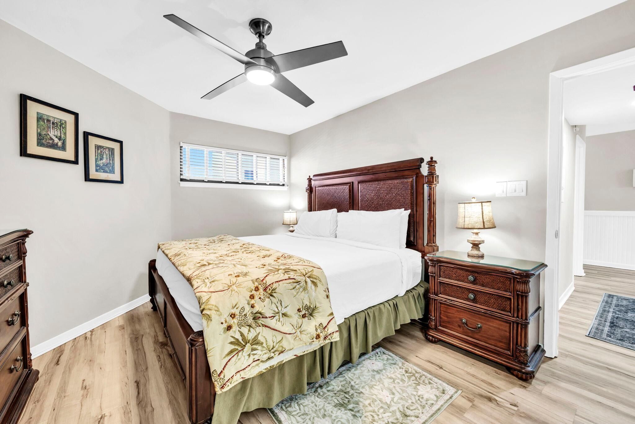 A bedroom with a bed, a nightstand, a dresser, a ceiling fan, and a window with blinds.