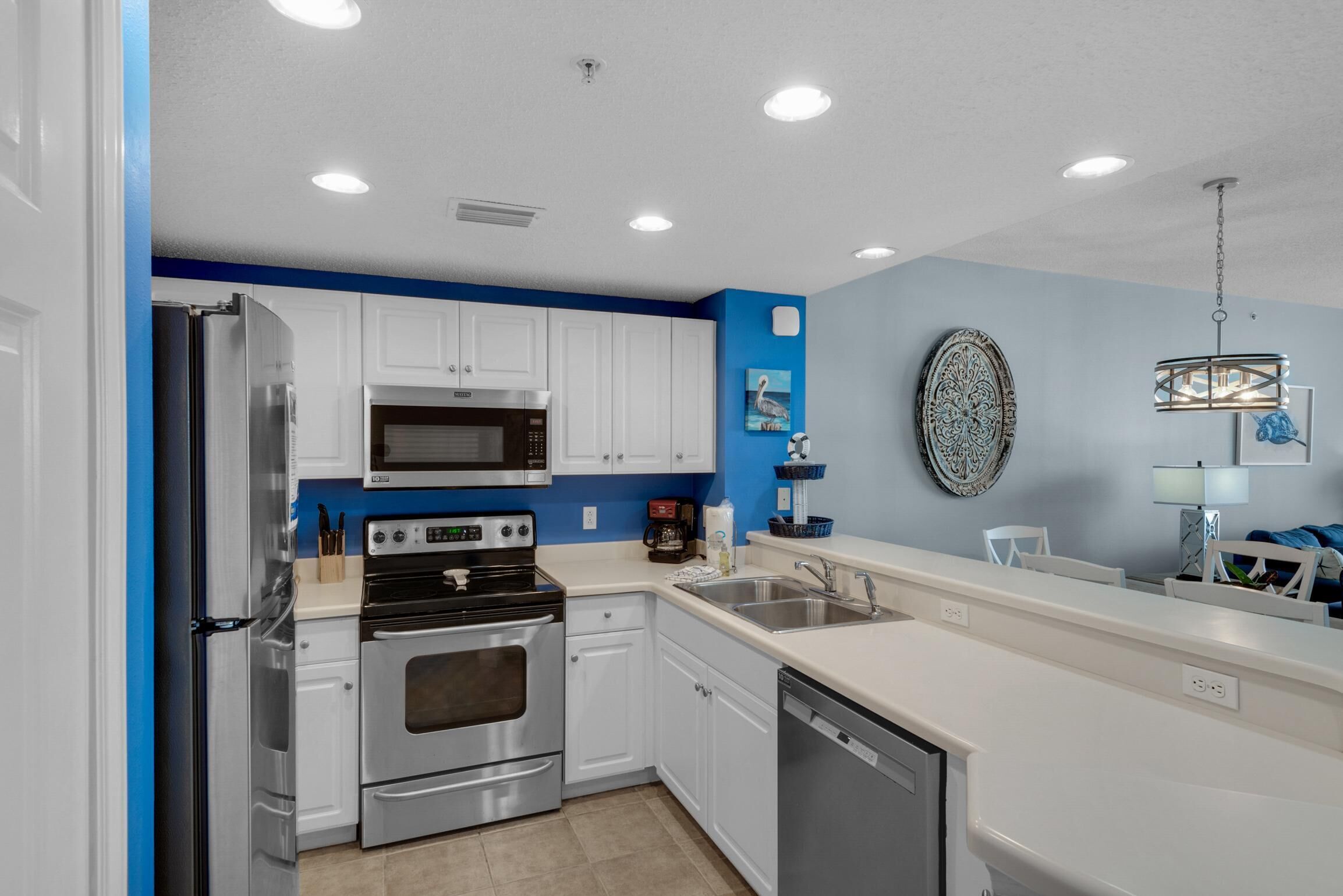A modern kitchen with white cabinets, stainless steel appliances, a blue accent wall, and a hanging light fixture.