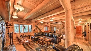 A log cabin interior with a stone fireplace, leather furniture, and wooden beams. - The 'Cool Creek Ranch' w/ 95 Acres on Yaak River (Troy)