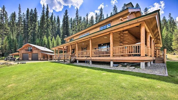 A log cabin with a porch, a separate garage, and a well-maintained lawn. - The 'Cool Creek Ranch' w/ 95 Acres on Yaak River (Troy)