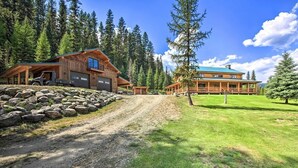 A large log cabin with a covered driveway and a separate building with a blue roof. - The 'Cool Creek Ranch' w/ 95 Acres on Yaak River (Troy)