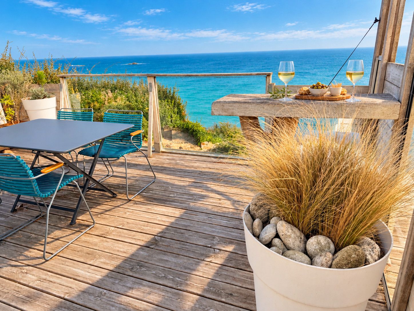 Een houten terras met een tafel en stoelen, met uitzicht op een heldere blauwe zee.
