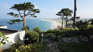 A coastal landscape with a view of the sea and beach, surrounded by trees and a stone pathway.