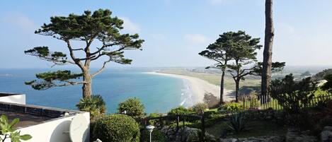 Un paisaje costero con vista al mar y a la playa, rodeado de árboles y un sendero de piedra.