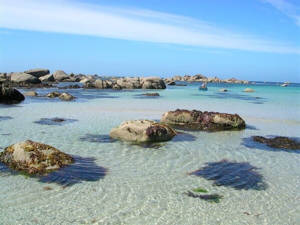 Een strand met helder turquoise water, grote rotsen en een boot in de verte.