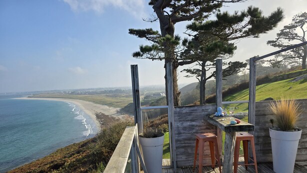 A wooden deck with a table and chairs overlooking a beach.