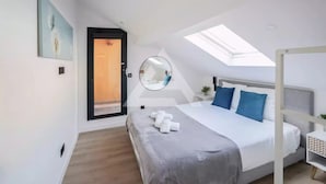 A modern bedroom with a skylight, a bed with blue and white pillows, a round mirror, and a door leading to an outdoor area. - Monaco Border - 100% new with see view (Beausoleil)