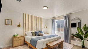 Ein Schlafzimmer mit einem hölzernen Bett, Nachttischen, einer Bank, einem großen Spiegel und einer Topfpflanze.