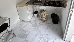 Eine kompakte Küche mit einem weißen Kühlschrank, einer Spüle, einem Herd und einer kleinen Mülltonne.
