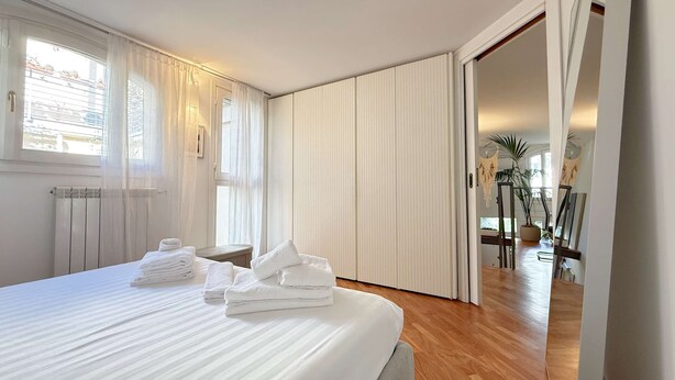 A hotel room with a large bed, a radiator, a window with curtains, and a view of a balcony with plants. - Loft Nicholas in Milano (Milan)
