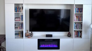 Moderni olohuone, jossa on suuri, seinälle asennettu litteänäyttöinen televisio. Sen alla on valkoinen TV-taso, ja molemmin puolin on kirjahyllyt.