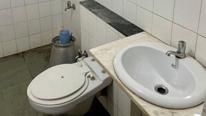 A bathroom with white tiles, a toilet, a sink, and a window with a diamond pattern. - The Imperial Heritage (Lonavala)