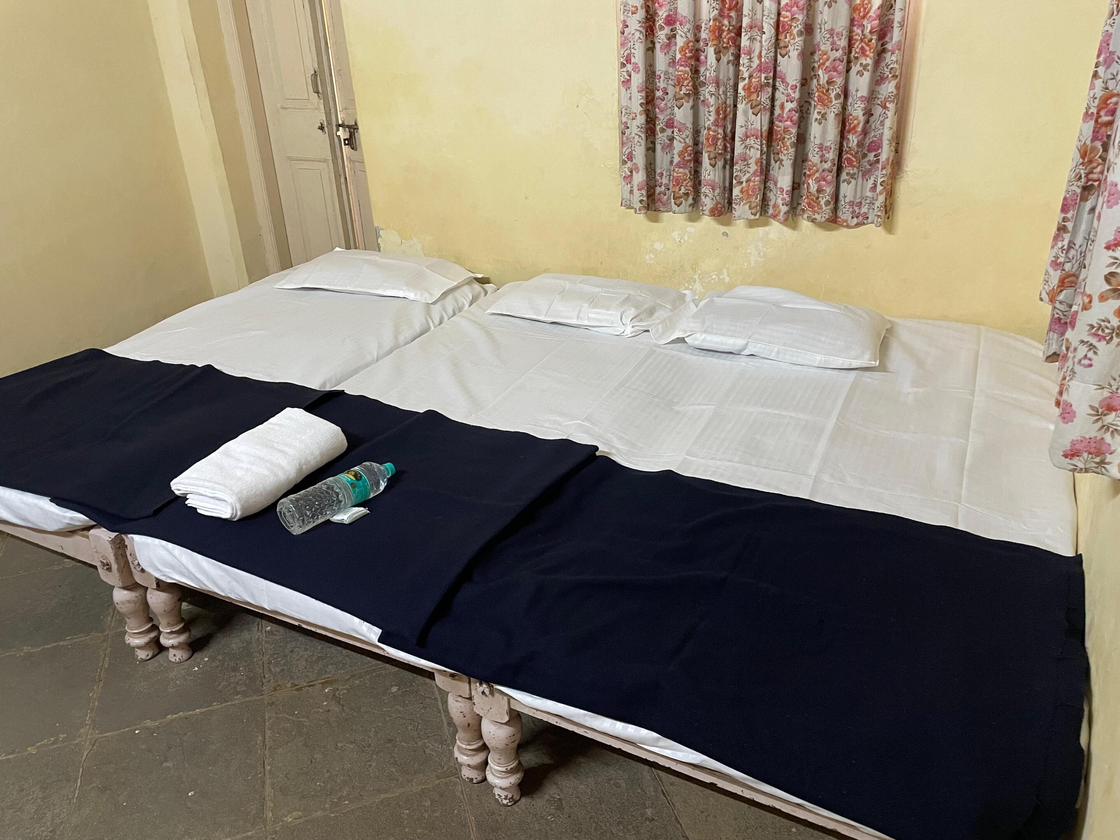 Cama doble con sábanas blancas, colcha azul oscuro y una toalla doblada. Una botella de agua y un objeto pequeño están sobre la cama.