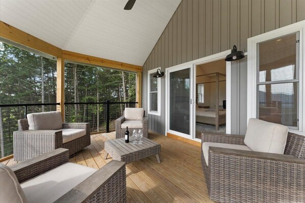 A covered outdoor area with wicker furniture, a bottle of wine, and a glass set on a table. - Large Estate, Spectacular Views, Hot Tub, Sauna, Game Room, Fireplace, Wet Bar (Bolton Landing)