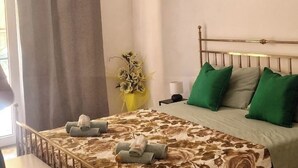 Een opgemaakt bed met een bloemenbedekking, groene en grijze kussens en handdoeken ernaast.