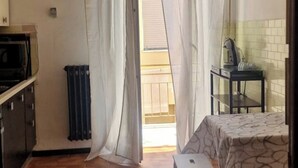 Een kleine, goed verlichte kamer met een bed, een tafel met een waterkoker en een radiator.