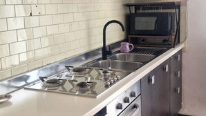 Een keuken met een gasfornuis, een spoelbak, een magnetron en kastjes.