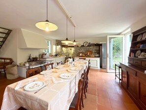 A spacious kitchen with a long dining table set for six, a stone wall backsplash, and a large window. - Casale Bera Hills View Private Pool and Garden (Cossano Belbo)