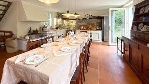 A spacious kitchen with a long dining table set for six, featuring white tablecloths and floral plates. - Casale Bera Hills View Private Pool and Garden (Cossano Belbo)