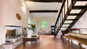 A spacious living room with a fireplace, a wooden staircase, and a view of the outdoors. - Casale Bera Hills View Private Pool and Garden (Cossano Belbo)