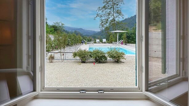 A clear view of a swimming pool with lounge chairs and umbrellas, surrounded by trees and a mountainous landscape. - Casale Bera Hills View Private Pool and Garden (Cossano Belbo)