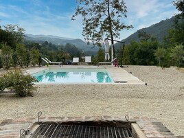 Una piscina con solárium de grava, rodeada de sillas de descanso y una zona de barbacoa.