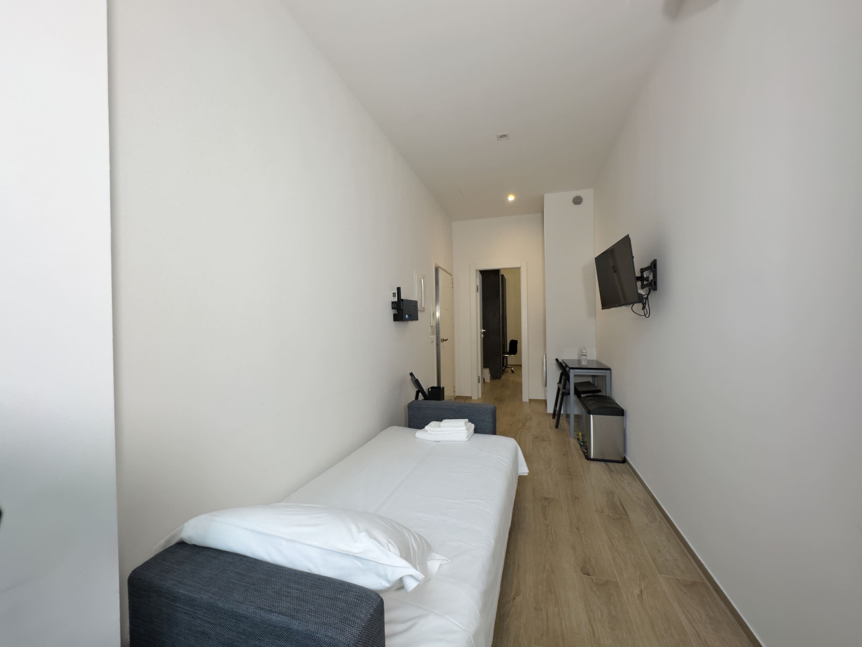 Una habitación de hotel pequeña y moderna con una cama individual, un escritorio y un televisor montado en la pared.