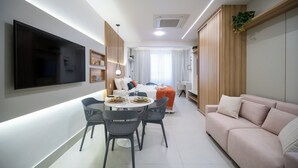 Un salon moderne doté d’un téléviseur à écran plat, d’une table à manger avec des chaises, d’un canapé et d’une grande fenêtre agrémentée de rideaux.