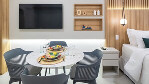 Une chambre d’hôtel moderne dotée d’un coin repas, d’un téléviseur à écran plat, d’étagères en bois et d’un lit avec une literie blanche.