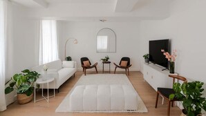A modern living room with a white sofa, two armchairs, a white rug, a TV, and potted plants. - The Portland - Marylebone - by Frankie (London)