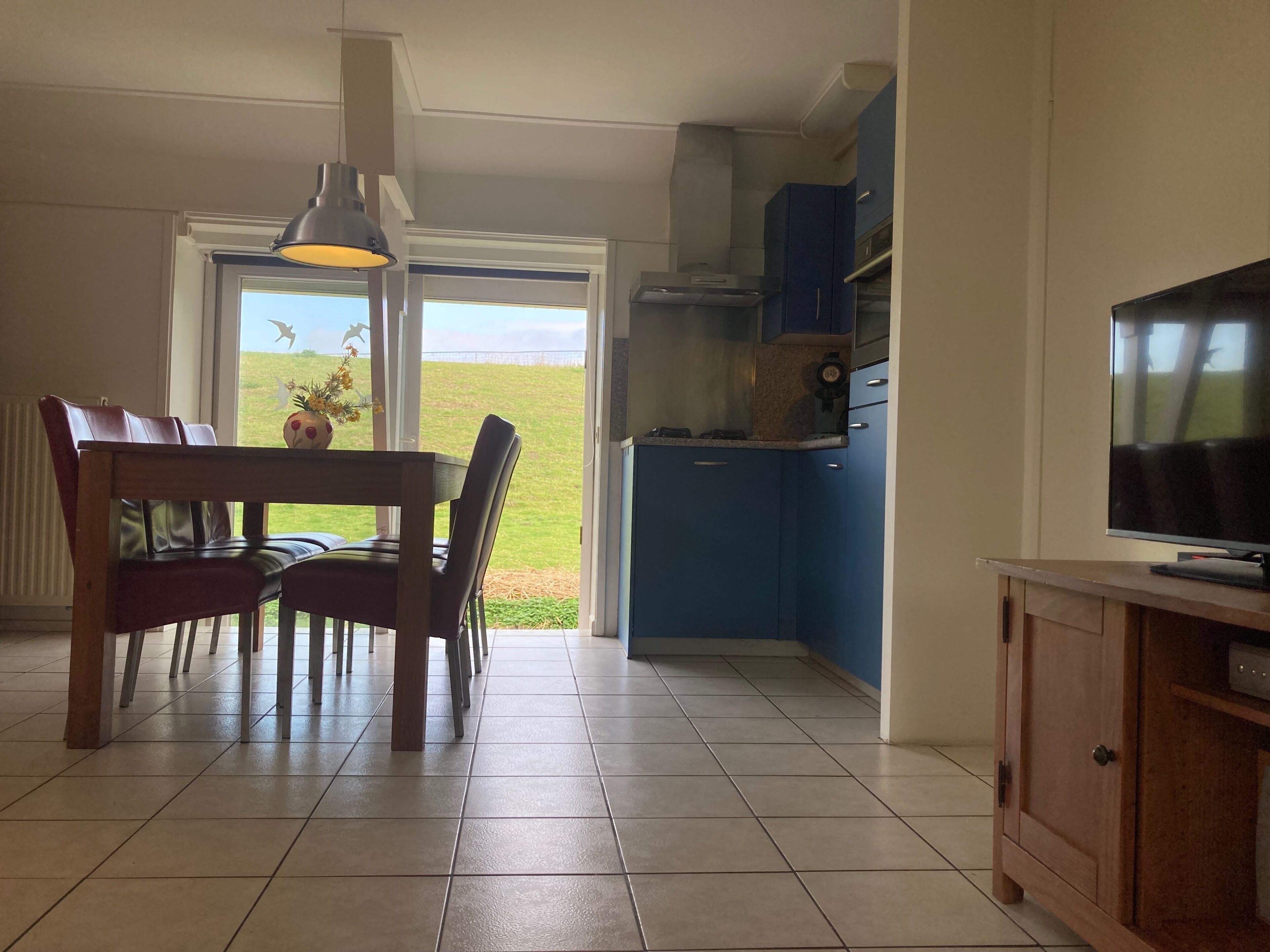 Ein Essbereich mit Tisch und Stühlen, einem Fernseher auf einem Schrank und einer Küchenzeile mit Schränken und einem Herd.