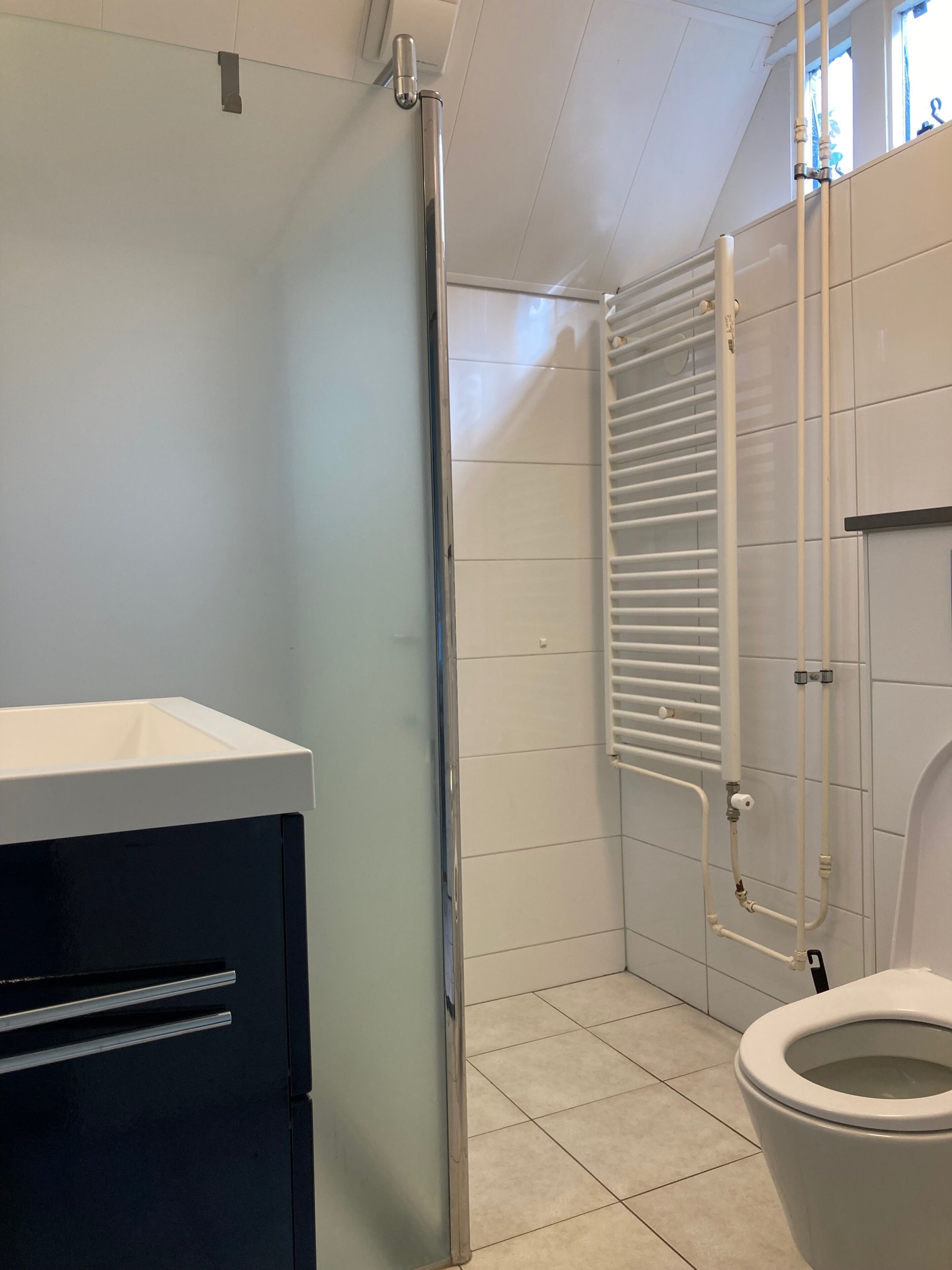 Un baño con inodoro, cabina de ducha de vidrio, radiador blanco y un mueble negro.