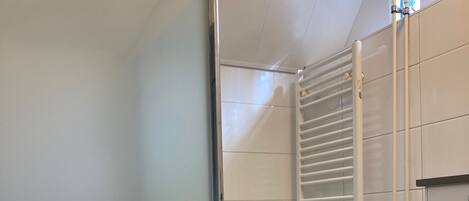 Un baño con inodoro, cabina de ducha de vidrio, radiador blanco y un mueble negro.